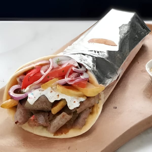 A Sammy's Touch gyro with meat, fries, tomatoes, onions, and white sauce, partially wrapped in foil.