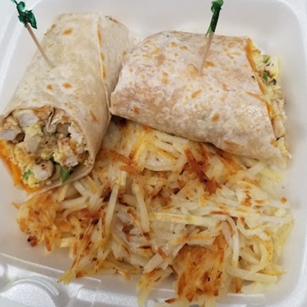 Two breakfast burritos with hash browns in a white takeout container from Sammy's Touch.