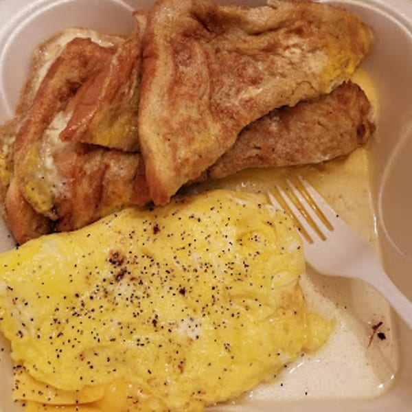 Scrambled eggs with pepper and three pieces of French toast in a white takeout container.