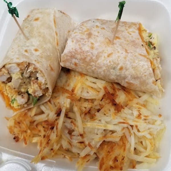 Two breakfast burritos with green picks, served with a side of crispy hash browns in a white container.