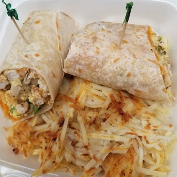 Two breakfast burritos with green picks, served alongside a pile of crispy hash browns.