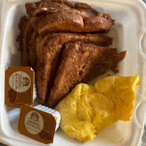 French toast, scrambled eggs, and two syrup packets in a white takeout container.