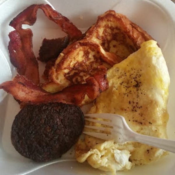 A breakfast plate with French toast, scrambled eggs, bacon, and a dark brown patty.