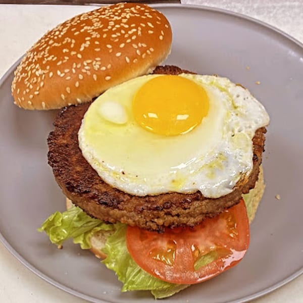 A Sammy's Touch burger with a fried egg, lettuce, and tomato on a sesame seed bun.