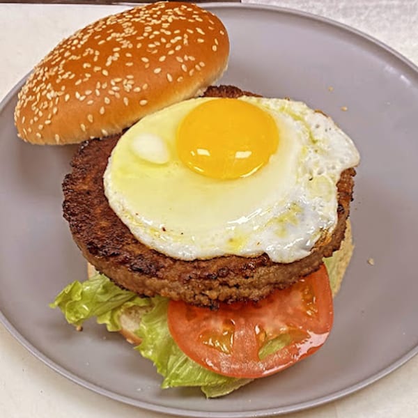 A Sammy's Touch burger with a fried egg, lettuce, and tomato on a sesame seed bun.