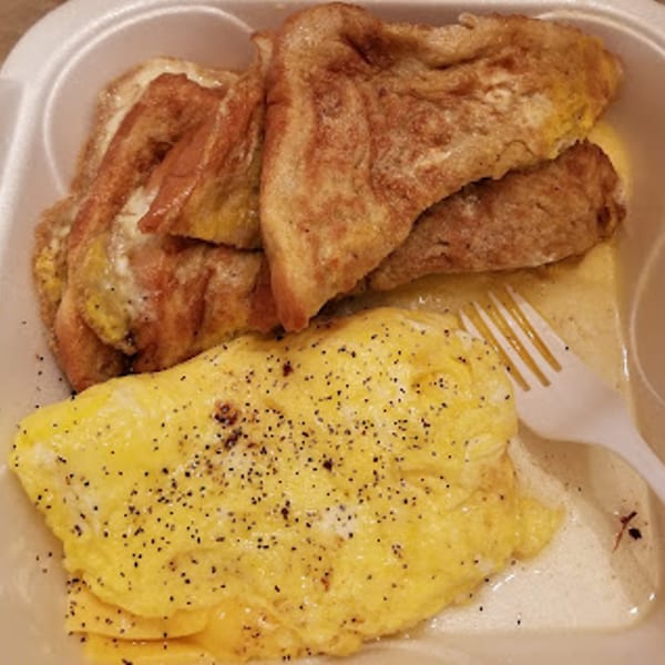 French toast and scrambled eggs with pepper in a white takeout container with a plastic fork.