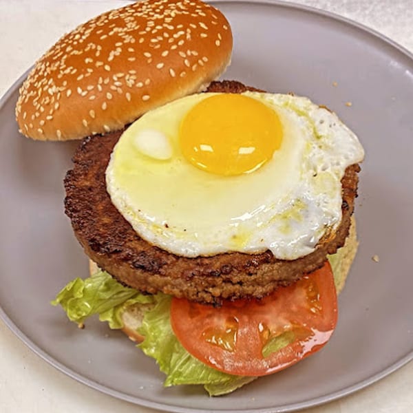 A Sammy's Touch burger with a patty, fried egg, lettuce, tomato, and a sesame seed bun.