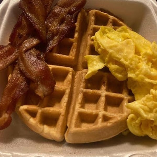 Sammy's Touch breakfast with crispy bacon, two waffles, and fluffy scrambled eggs in a takeout container.