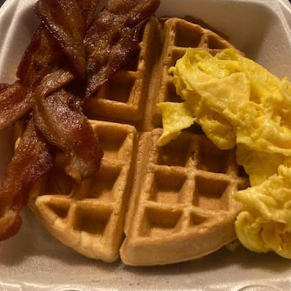 Sammy's Touch breakfast with crispy bacon, two waffles, and fluffy scrambled eggs in a takeout container.